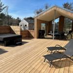 Terrasse mit Liegestühlen, Grill und Whirlpool. Holzdeck und Sicht auf Wald.