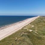 Strand mit Dünen und Häusern am Meer unter blauem Himmel