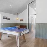 Tischtennisplatte im Raum mit Holzboden und Wandpaneelen. Durchgang zur Terrasse mit Außensitzgelegenheit.