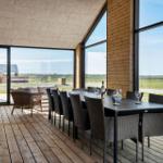 Terrasse mit Esstisch und Stühlen. Große Fenster bieten Blick auf Felder.