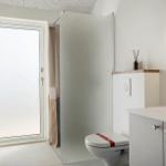Badezimmer mit Toilette, Waschbecken und Dusche. Fenster mit Milchglas und runder Spiegel.