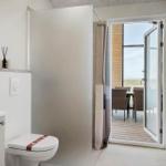 Badezimmer mit Toilette und Dusche. Durchgehendes Fenster zum Balkon mit Sitzgelegenheiten.