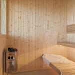 Sauna mit Holzwand, Bank und Heizgerät. Fenster zeigt Himmel.