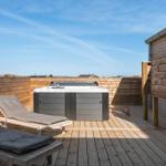 Terrasse mit Whirlpool, Sonnenliegen und Holzwand. Dachüberdachung und Dusche vorhanden.
