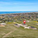 Aerial view of a coastal village with modern houses and a red location marker.