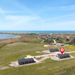 Modernes Ferienhaus auf grünem Grundstück mit Blick aufs Meer und Windkraftanlagen.