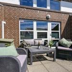 Terrasse mit Sitzgruppe, Tisch und Grill. Hintergrund: Backsteinmauer und Fenster.