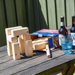 Holzbausteine, zwei Bierflaschen und ein Glas auf einer Holzbank im Freien.