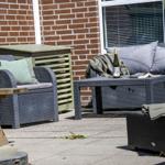 Terrasse mit Gartenmöbeln, Tisch und Weinflasche vor Backsteinmauer.