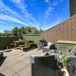 Terrasse mit Sitzgruppe, Grill und Picknicktisch. Hinterhof mit grünem Zaun und Garten.
