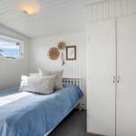 Schlafzimmer mit Bett, Kleiderschrank und Fenster. Wände und Decke weiß verkleidet.