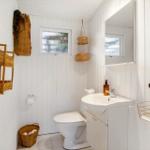 Badezimmer mit Toilette, Waschbecken und Dusche. Wandverkleidung weiß, Körbe aus Rattan.