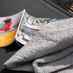 Zwei Zeitschriften und eine gestreifte Decke liegen auf einer Außenterrassenbank.