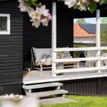 Terrasse mit Liegestuhl und Blumen vor schwarzem Holzhaus