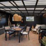 Terrasse mit Tisch, Stühlen, Grill und Hängelampe unter schwarzem Dach.