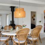 Rattan-Stühle um einen runden Tisch mit Decken und Vasen. Hängelampe und Kamin im Hintergrund.