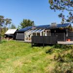 Schwarzes Haus mit Solaranlage und Terrasse im Grünen.