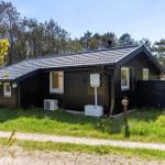 Ein dunkles Holzhaus mit Dach und Fenstern steht im Gras vor einem Wald.