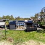 Schwarze Holzhütte mit Glasveranda und Solarpanel auf Dach. Umgeben von Gras und Bäumen.