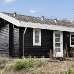 Black wooden house with white windows and door under blue sky.