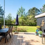 Wooden terrace with table, chairs, and umbrella. Green areas and trees in the background.