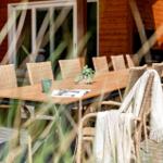 Lange Holzterrasse mit Esstisch und Stühlen, Blick auf Holzhaus im Hintergrund.
