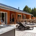 Holzhaus mit Terrasse, Liegen, Tisch und Stühlen sowie Whirlpool im Vordergrund.