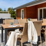 Terrasse mit Esstisch, Stühlen und Decken. Hintergrund: Holzhaus und Grillbereich.