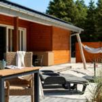 Terrasse mit Tisch, Stühlen, Liegen und Hängematten vor Holzhäusern.