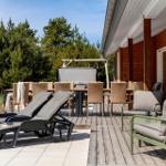 Terrasse mit Liegestühlen, Tisch und Stühlen, Holzwand und Grill unter Bäumen.