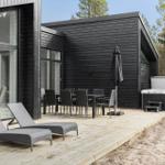 Terrasse mit Liegestühlen, Tisch, Stühlen und Whirlpool neben modernem Haus.