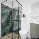 Badezimmer mit Dusche, Toilette und Waschbecken. Duschwand aus grünem Marmor.