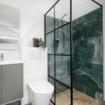 Badezimmer mit Dusche, Waschbecken und Toilette. Grün gemasertes Mosaik an der Wand.