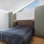 Schlafzimmer mit Bett, Holzfußboden und großen Fenstern.