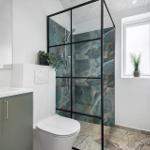 Badezimmer mit Dusche, Waschbecken und Toilette. Fenster mit Pflanze.