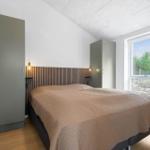 Schlafzimmer mit Bett, Kleiderschrank und Fenster mit Blick auf Wald.