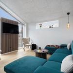 Ein Wohnzimmer mit blauem Sofa, Fernseher und großem Fenster. Helle Wände und Holzboden.