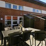 Terrasse mit Tisch und Stühlen vor einem Backsteinhaus mit Fenstern und Sonnenschutz.