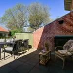 Terrasse mit Esstisch, Stühlen und Sitzgelegenheit an Backsteinwand.