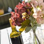 Auf dem Tisch steht eine Blumenvase mit roten und rosa Hortensien, eine Weinflasche und eine Kerze.