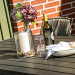 Außenbereich mit Tisch, Stühlen, Blumen, Kerze und Weinflasche.