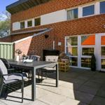 Terrasse mit Tisch, Stühlen und Sitzgelegenheit vor einem Backsteinhaus mit Eingangstür.