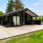 Modern wooden cabin with large deck, seating, and garden.