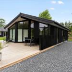 Modern wooden cabin with large deck, garden, and barbecue area.
