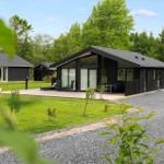 Modern wooden cabin with terrace and garden. Surrounded by trees and grass.