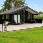 Modern wooden cabin with large terrace and garden. Garden furniture and plants are present.