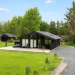 Modern black wooden cabin with large balcony and garden. Surrounded by trees and grass.