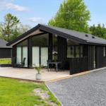 Modern black cabin with terrace, garden, and view of forest.