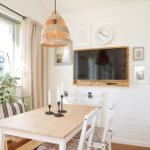 Dining room with wooden table, white chairs, and wall-mounted TV. Clock and pictures on the wall.