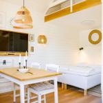 A room with a sleeping area, dining table, and TV mounted on the wall.